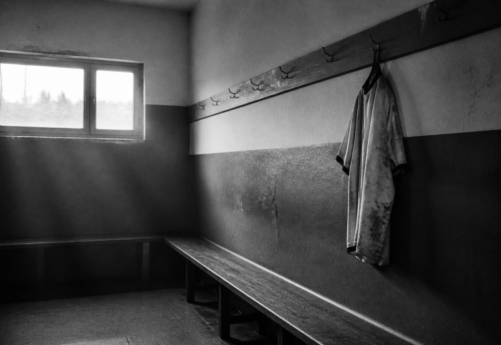 An empty changing room with a single worn football shirt hanging on a peg